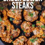 A skillet filled with crispy baked cauliflower steaks garnished with herbs and grated cheese, with lemon wedges at the edges.