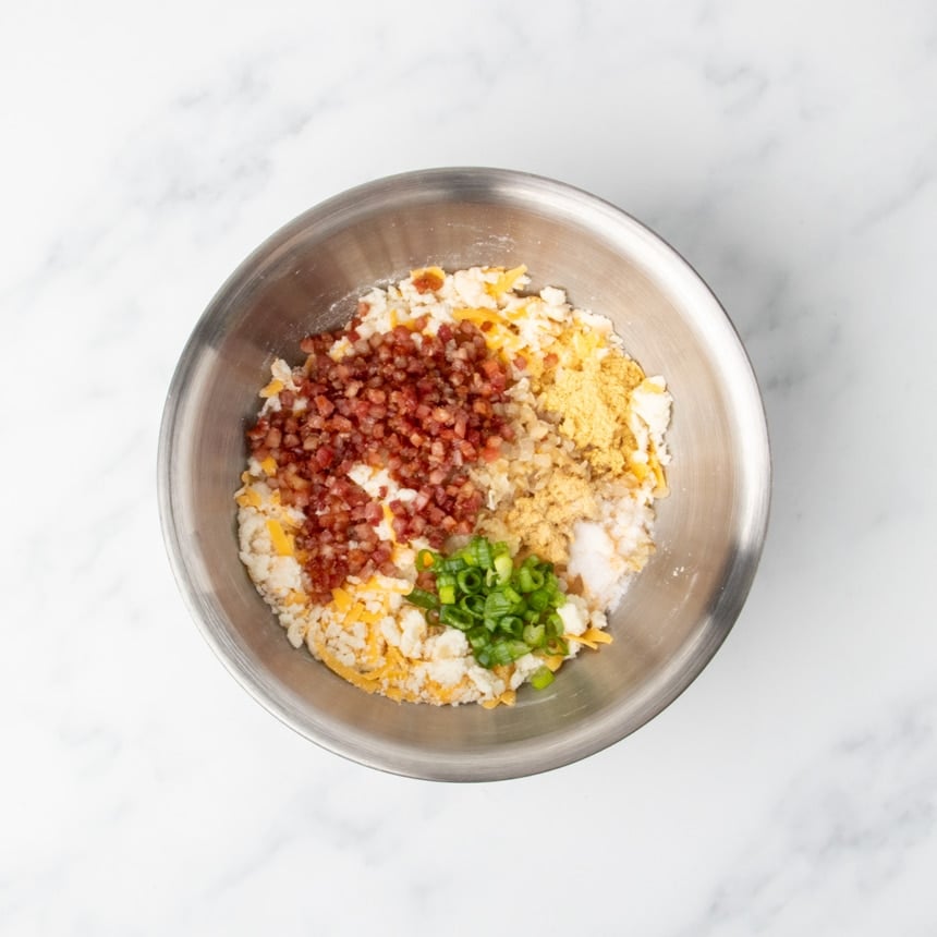 Cooked chopped pancetta and onions, chopped scallions, and seasonings on top of the cheese, potato and flour mixture in a stainless steel bowl.