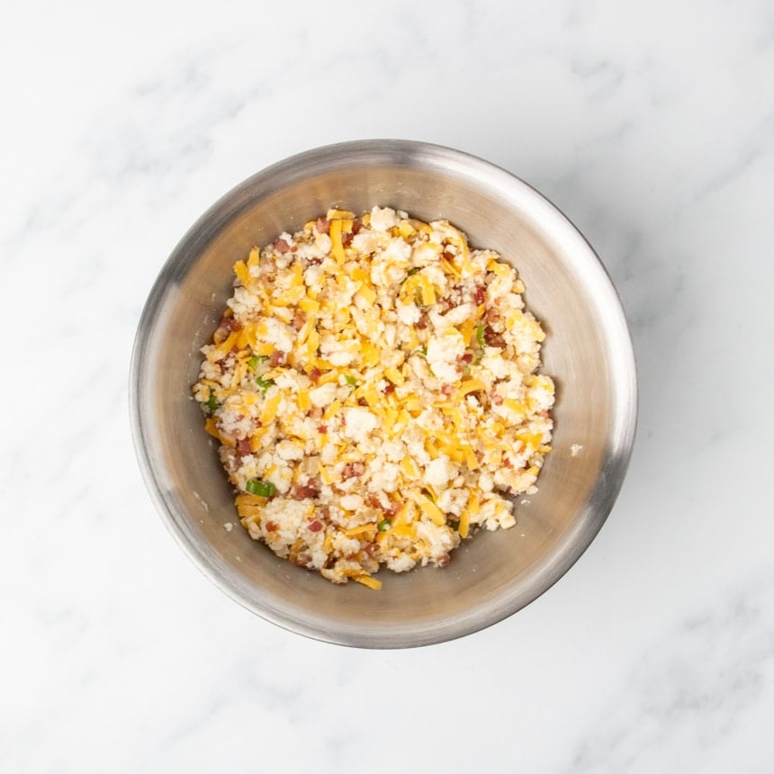 All ingredients mixed together into a crumbly mixture of cheese, onions, cooked pancett, potatoes, and scallions a in a stainless steel bowl.