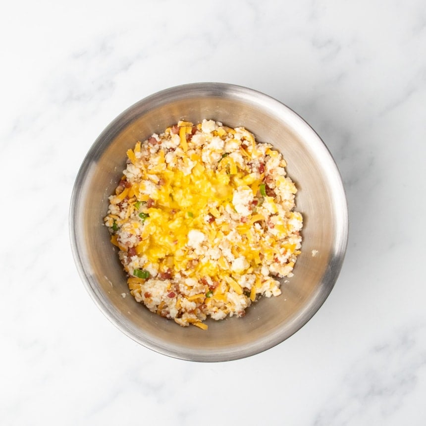 Same mixture with one beaten egg visible on top in a stainless steel bowl.