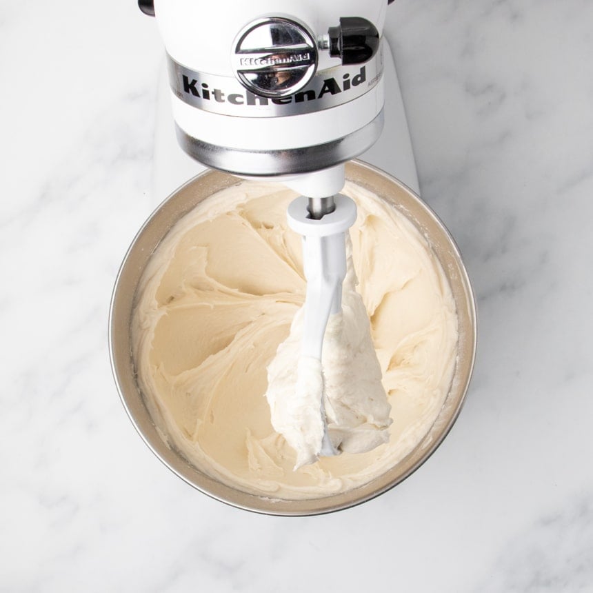 A stand mixer with a paddle attachment mixing dough until it is smooth and sticking to the inside of the bowl.