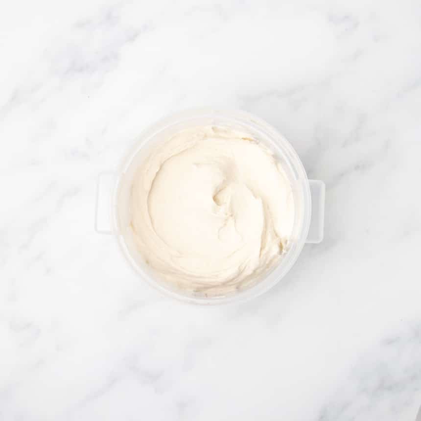 A plastic container filled with smooth, pale dough resting on a white marble surface.