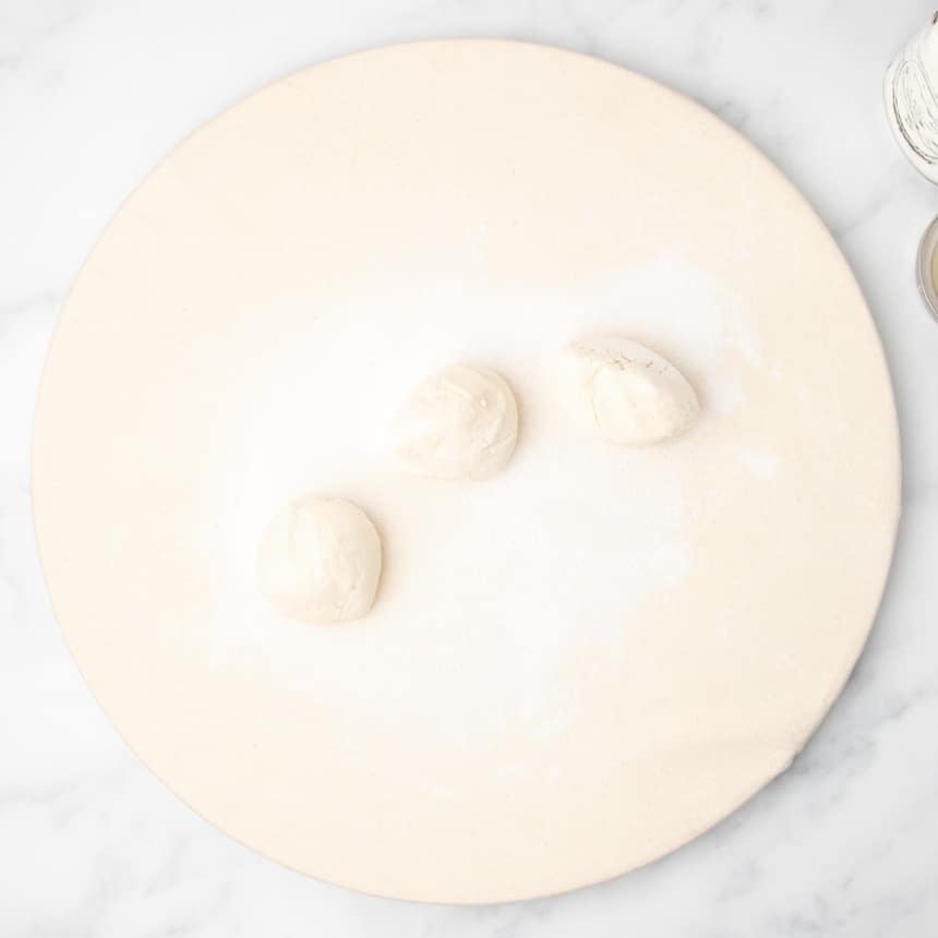 Three small portions of unshaped raw dough resting on a floured round canvas-covered surface.