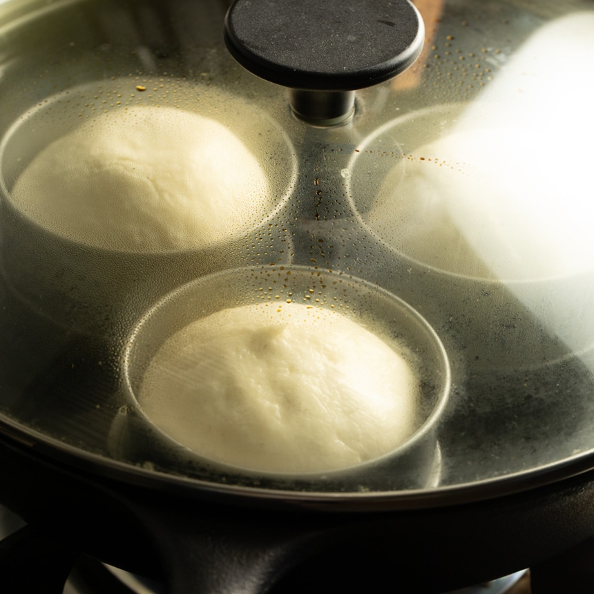 Risen dough portions visible through the glass lid of the skillet, showing steam and condensation inside.