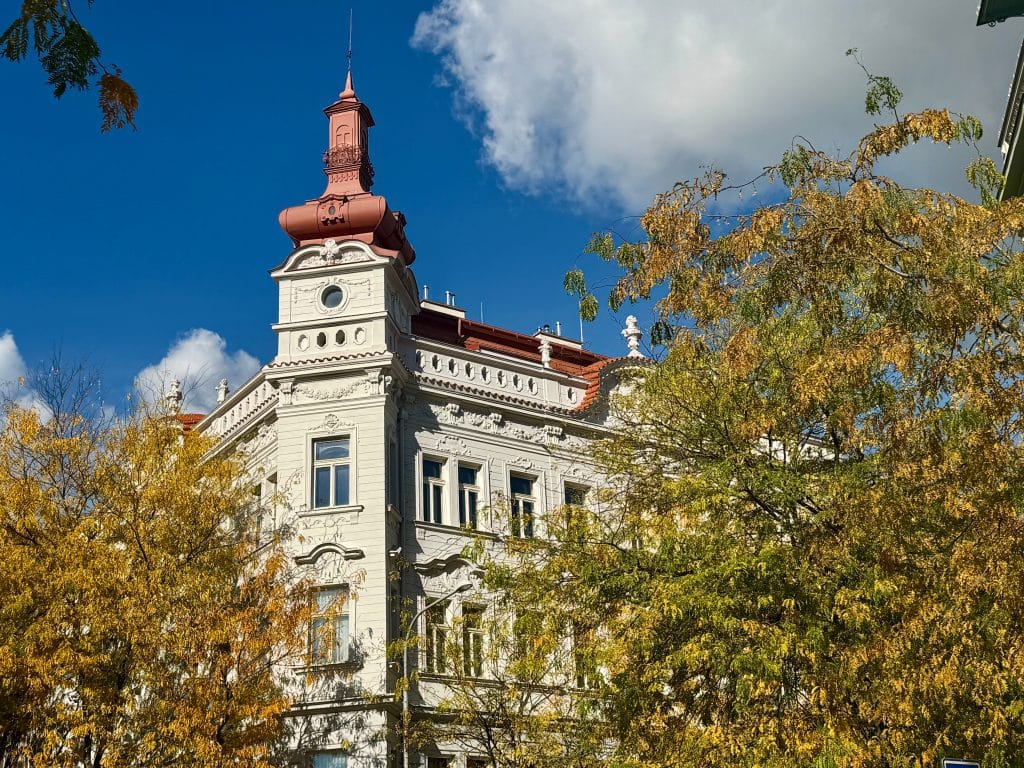 A tall white crenellated building in Prague, surrounded by yellow changing leaves