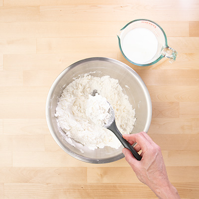 Hand holding black mixing spoon with grated butter mixed with dry ingredients.
