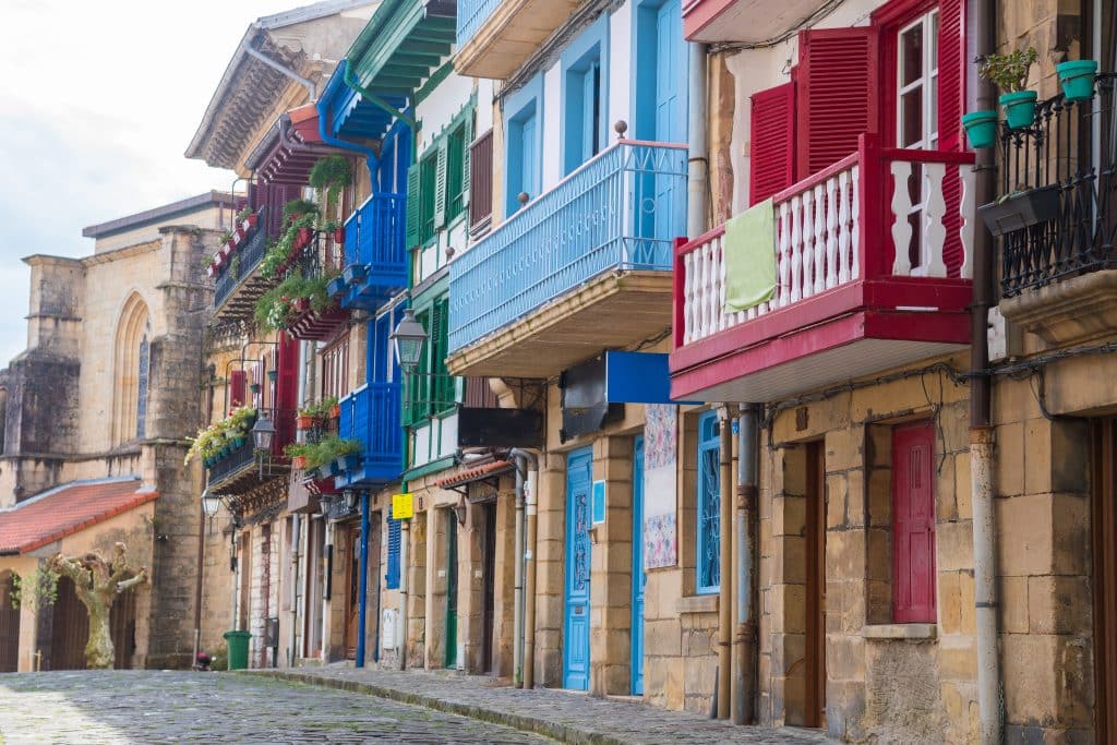 A small Basque town with bright blue and red wooden balconies on top of stone houses.