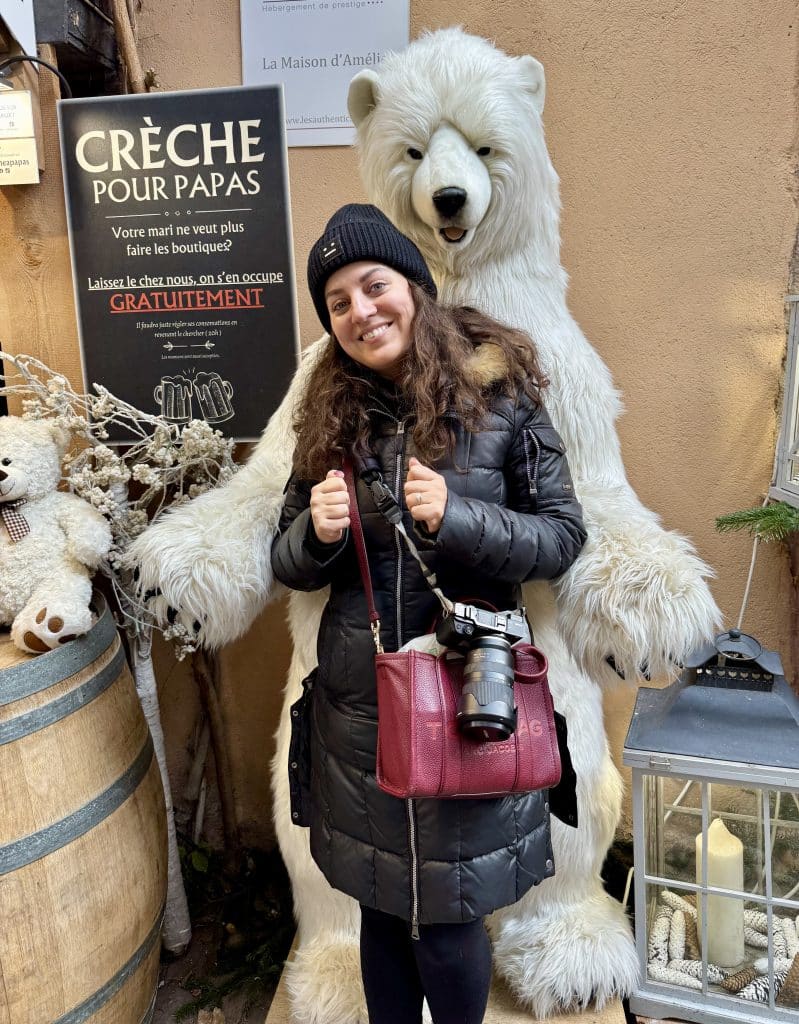 Kate dressed in a winter coat and hat while being spooned by a giant stuffed polar bear in France.