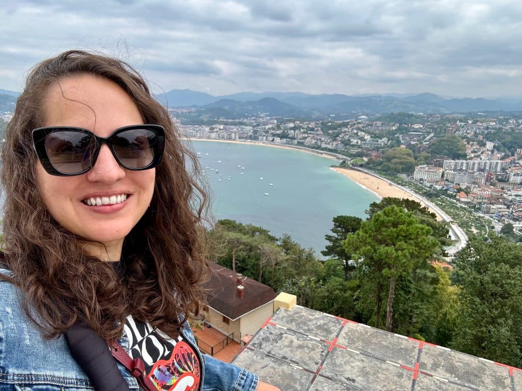 Kate taking a selfie in front of the view of the shell-shaped beach from far above.