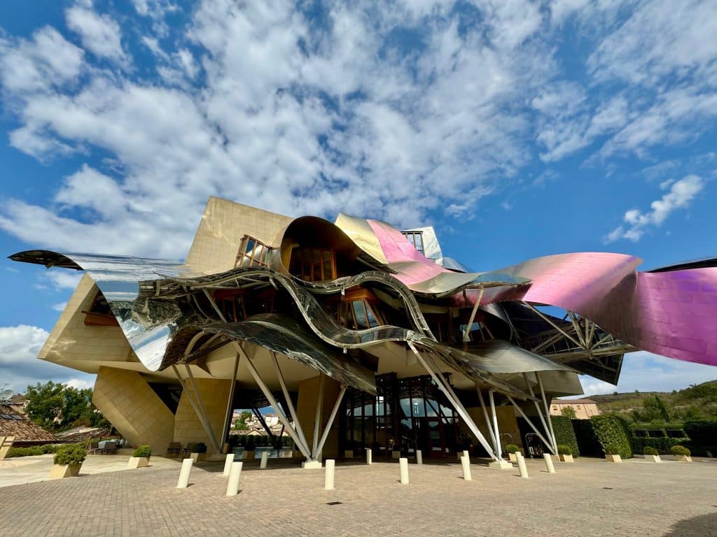 A winery with a roof that looks like curvy sheets of metal in pink, gold, and silver.