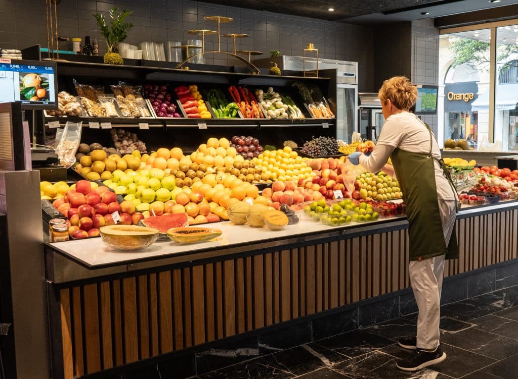A woman arranging a bunch of apples on a shelf in a market.