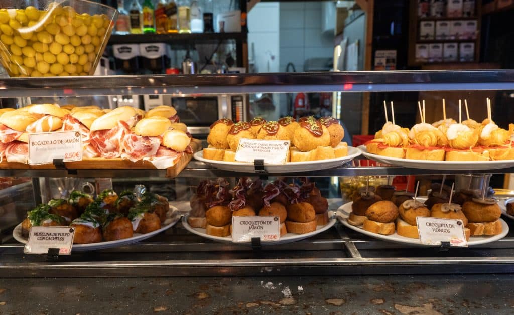 Six giant plates filled with dozens of pintxos behind a counter.