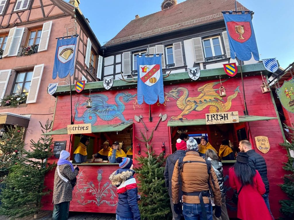 People buying crepes and Irish coffee at multicolored medieval wooden booths.