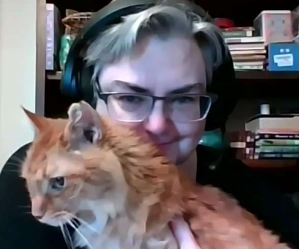Min, a longerhaired orange tabby on the lap of Sarah Jane, who has headphones and grey hair and glasses peeking over Min's back