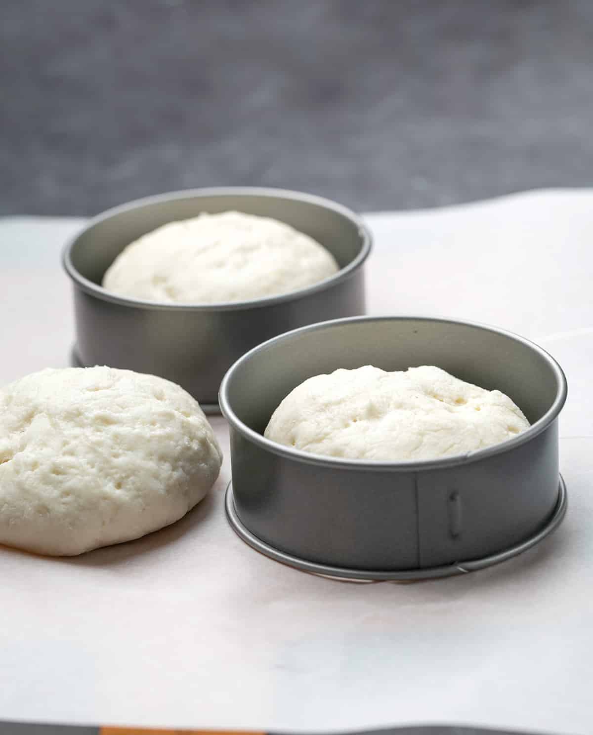 Three raw English muffins with 2 metal rings on white paper