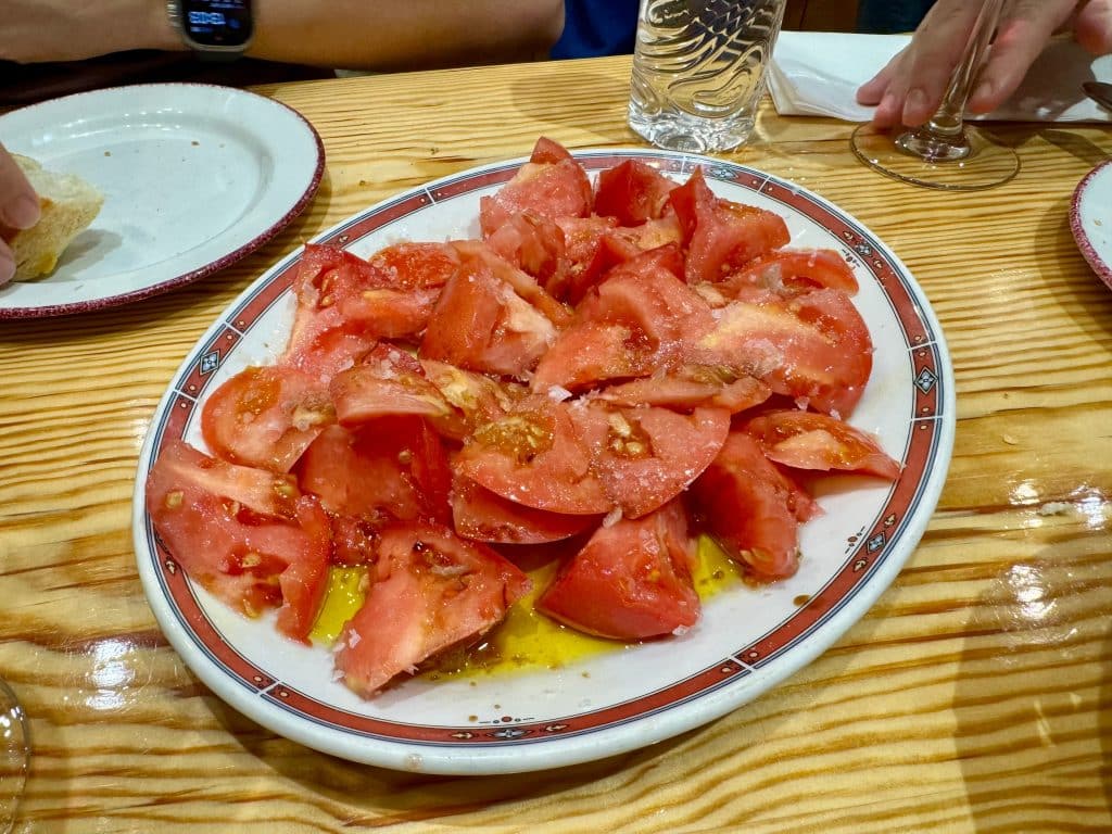 A huge plate of cut tomatoes covered in flaky sea salt and olive oil.