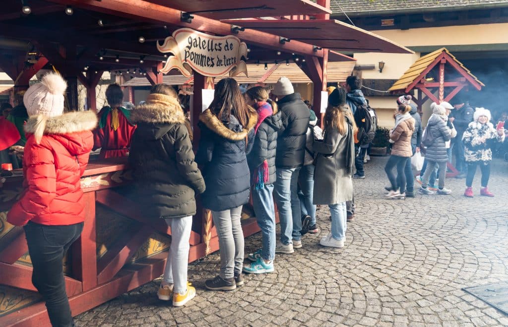 A line of women in puffy coats, hats, and skinny jeans standing in line at a Galettes de Pomme de Terre booth.