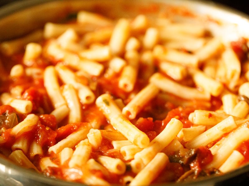 cooked ziti tossed with tomato sauce in pan