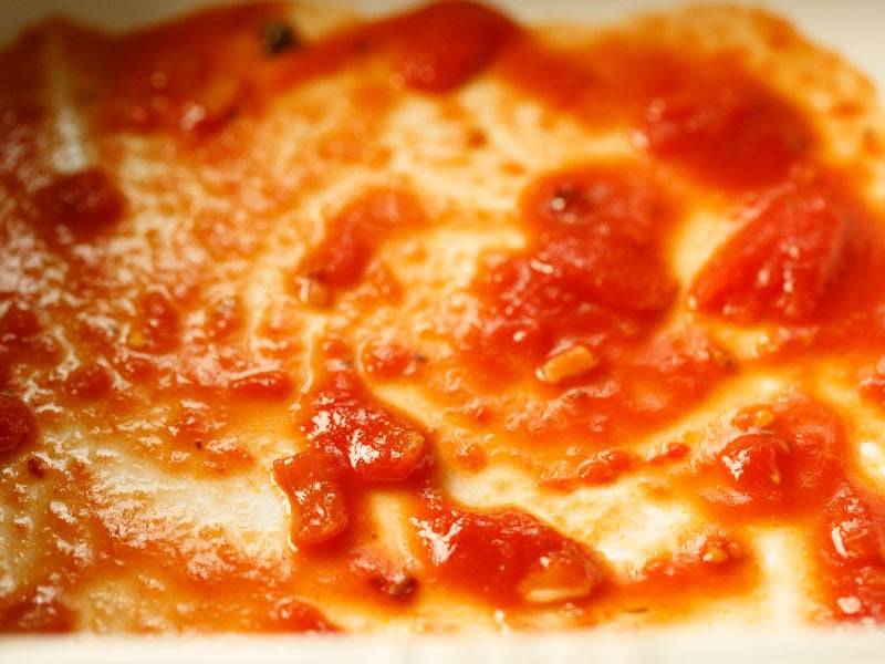 a few spoonfuls of tomato sauce spread out in the bottom of the casserole dish