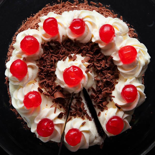 overhead shot of black forest cake on a black plate with a slice being removed.