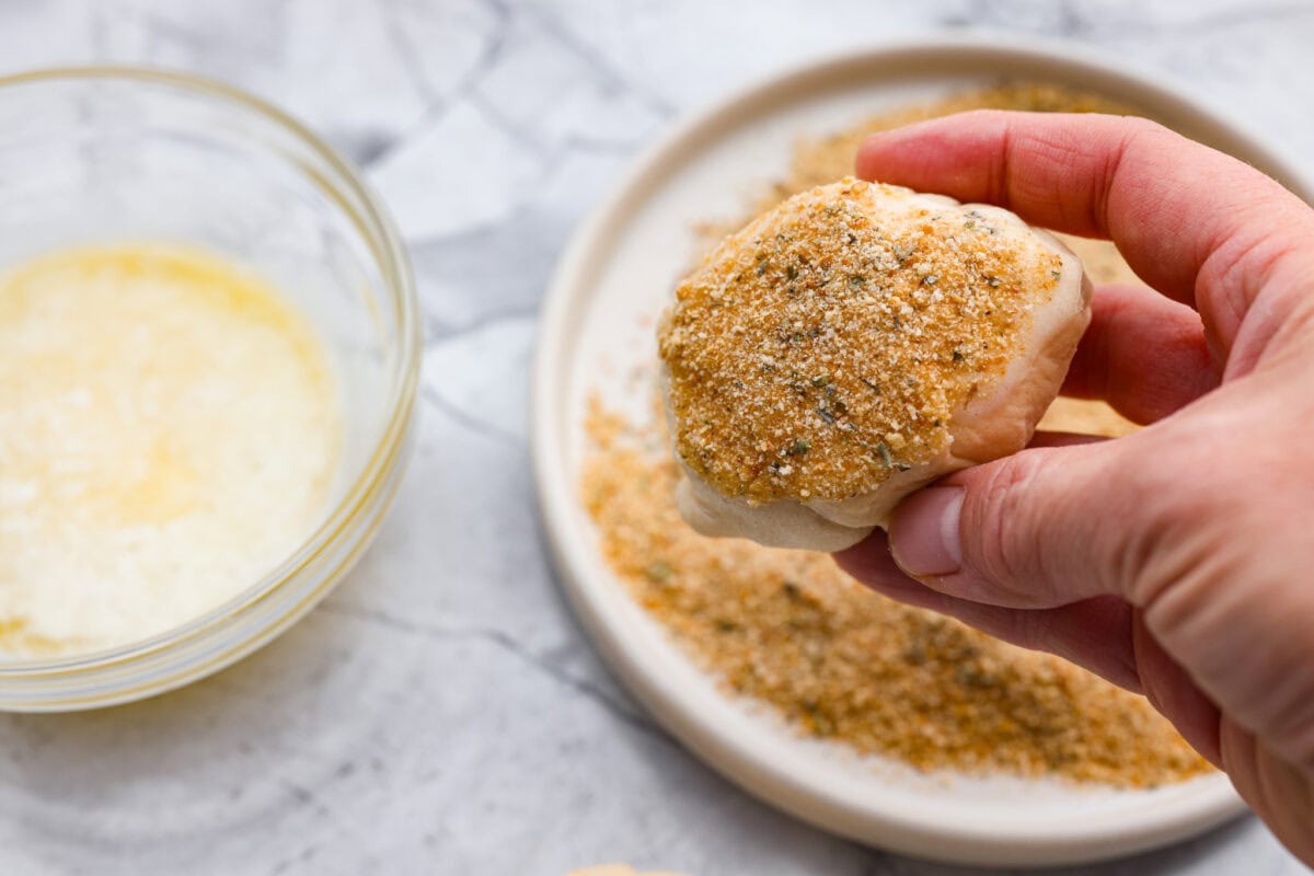 Someone coating the chicken pillows with butter and seasoned breadcrumbs. 
