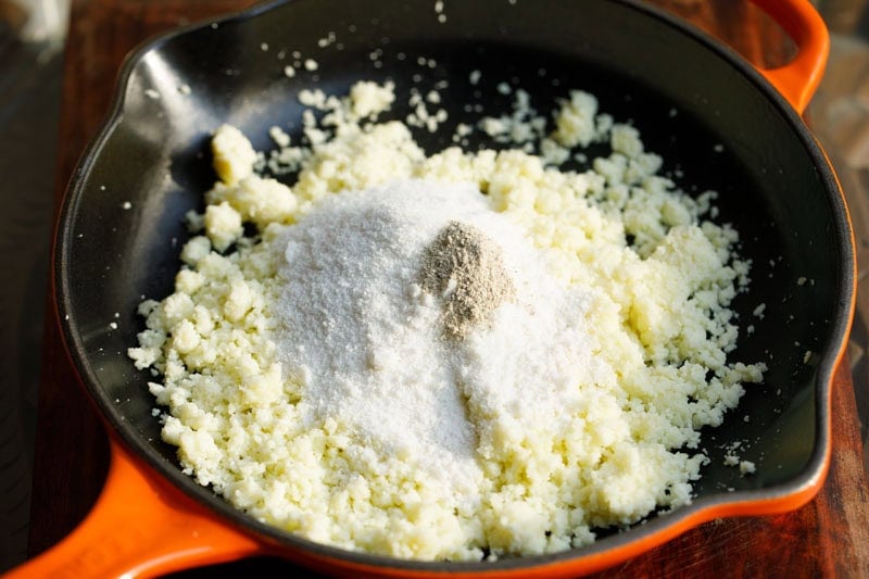 mound of powdered sugar with a bit of cardamom powder on sautéed mawa in skillet.