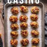 Overhead view of a tray with 16 baked clams casino on parchment paper, topped with bacon and herbs, on a gray striped cloth. Text reads "How to make Clams Casino.