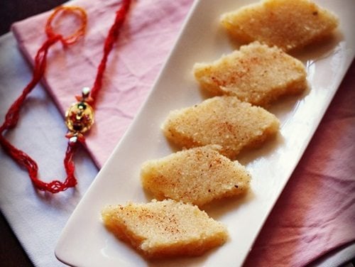 coconut burfi slices on a white platter with a rakhi in the background.