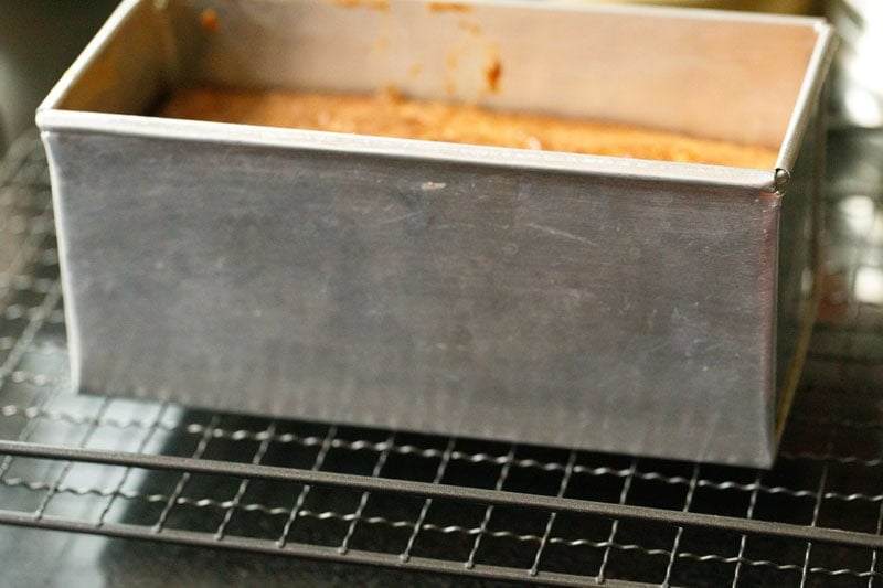 Metal loaf pan with baked cake on a wired rack.