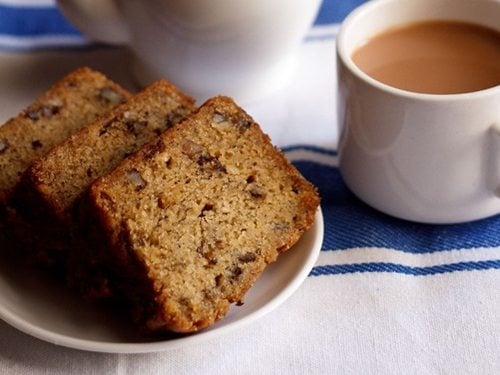eggless banana cake slices on plate with tea by the side.