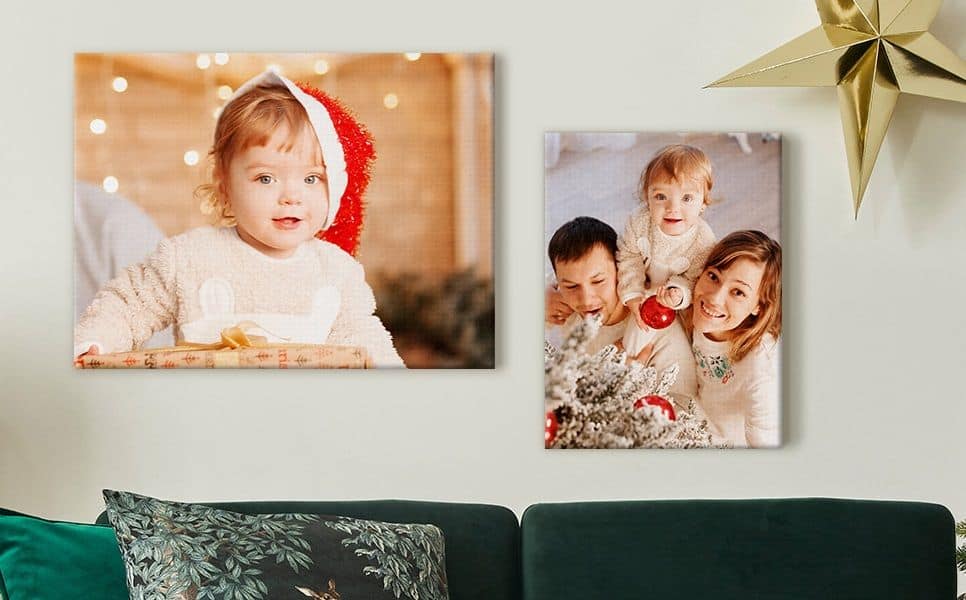 Christmas-themed family memory wall with two canvas prints—toddler in a Santa hat and family decorating a tree above a green sofa.