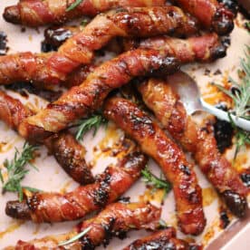 A tray of gluten free pigs in blankets with sprigs of rosemary.