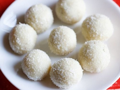 coconut ladoo placed in a circle and in the center on a white plate on a red table