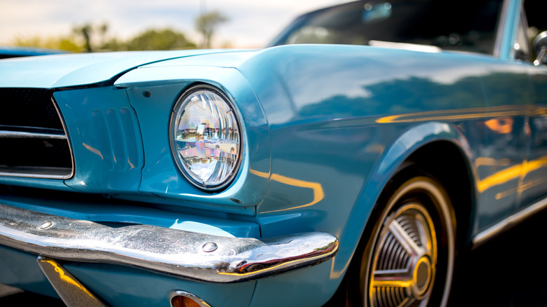 A blue classic Mustang with a shiny chrome front bumper