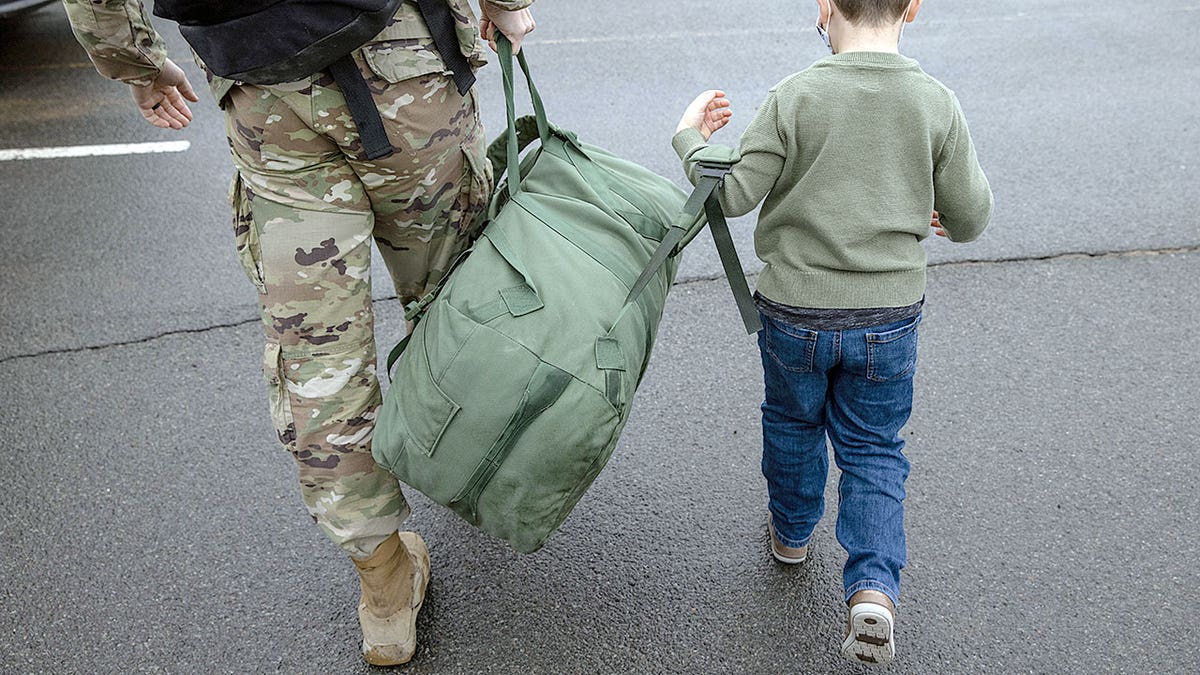 A child walks next to a soldier.