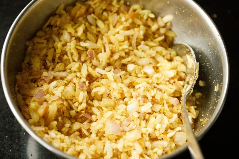 Bowl of evenly mixed flattened rice with onions and spices.