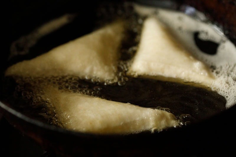 Frying onion samosa in hot oil in kadai.