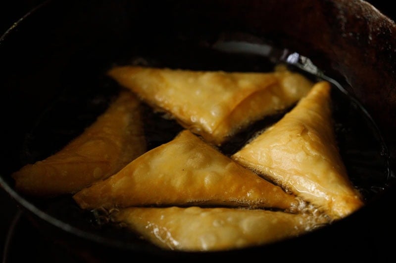 Fried light golden triangular onion samosa in oil.