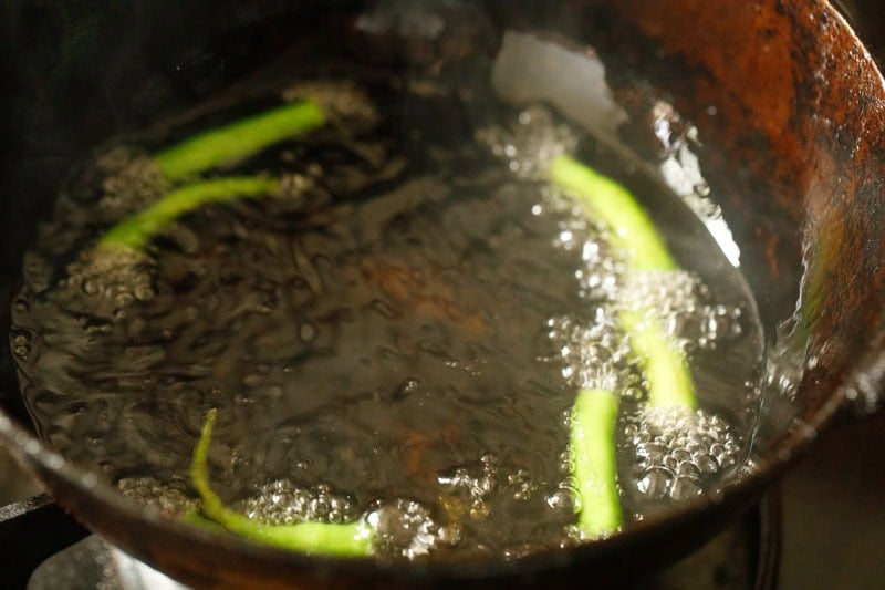Green chilies frying in oil in a kadai.