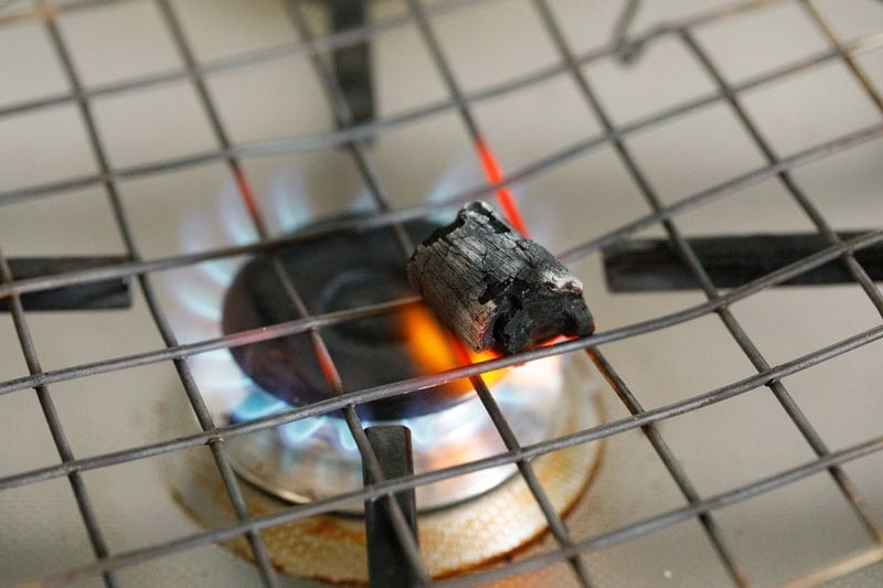 Small piece of charcoal kept on a flame proof rack on top of a lit stovetop.