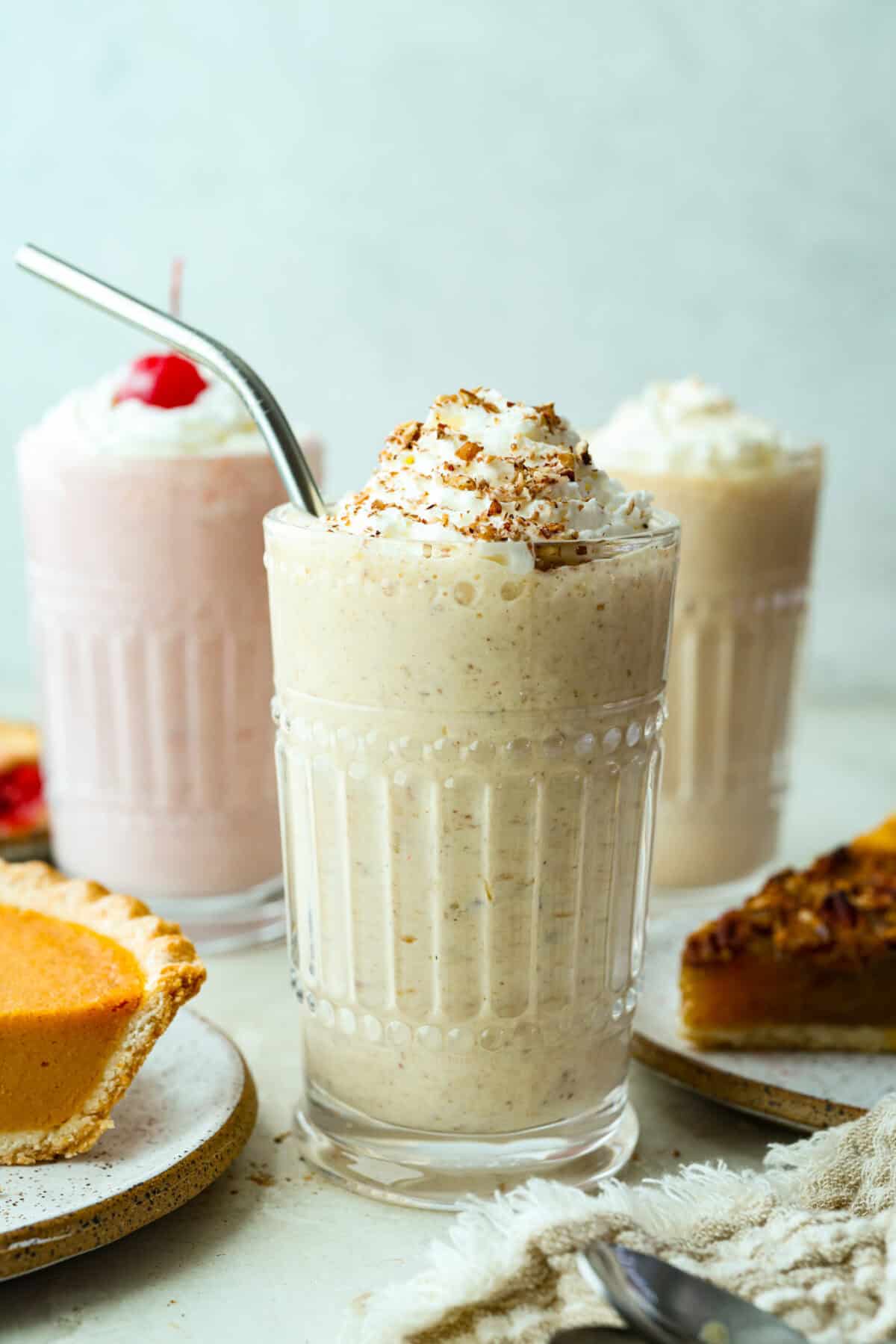 3 different pie milkshakes in cte decorative glasses next to slices of pie. 
