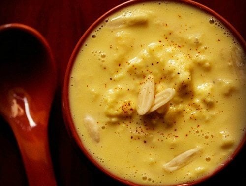 closeup shot of rabdi in red bowl with nuts and a light sprinkle of saffron powder from top