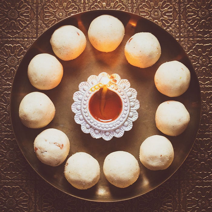 rava ladoo in a circle with lit earthern lamp in center on a bronze plate - diwali recipes.