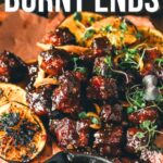 Maple chipotle bourbon glazed smoked pork belly burnt ends are served with grilled orange slices and fresh herbs on parchment paper for a deliciously smoky, sweet, and tangy bite.