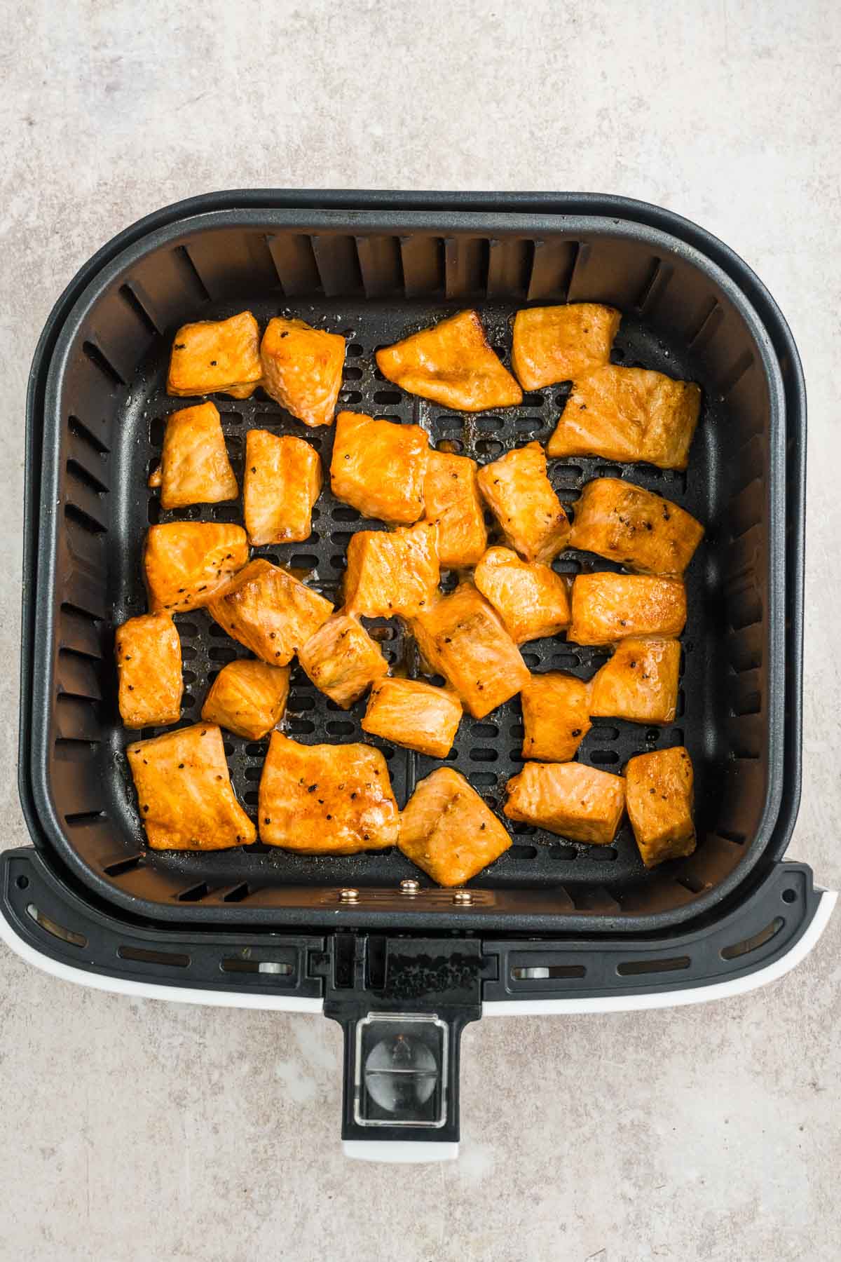 Cubed pieces of seasoned salmon are arranged in a single layer inside an air fryer basket.