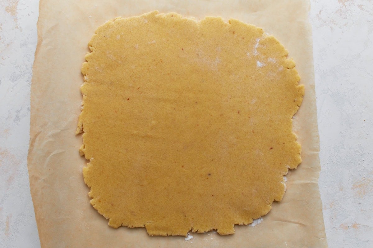 Chilled almond flour sugar cookie dough rolled out between parchment paper.