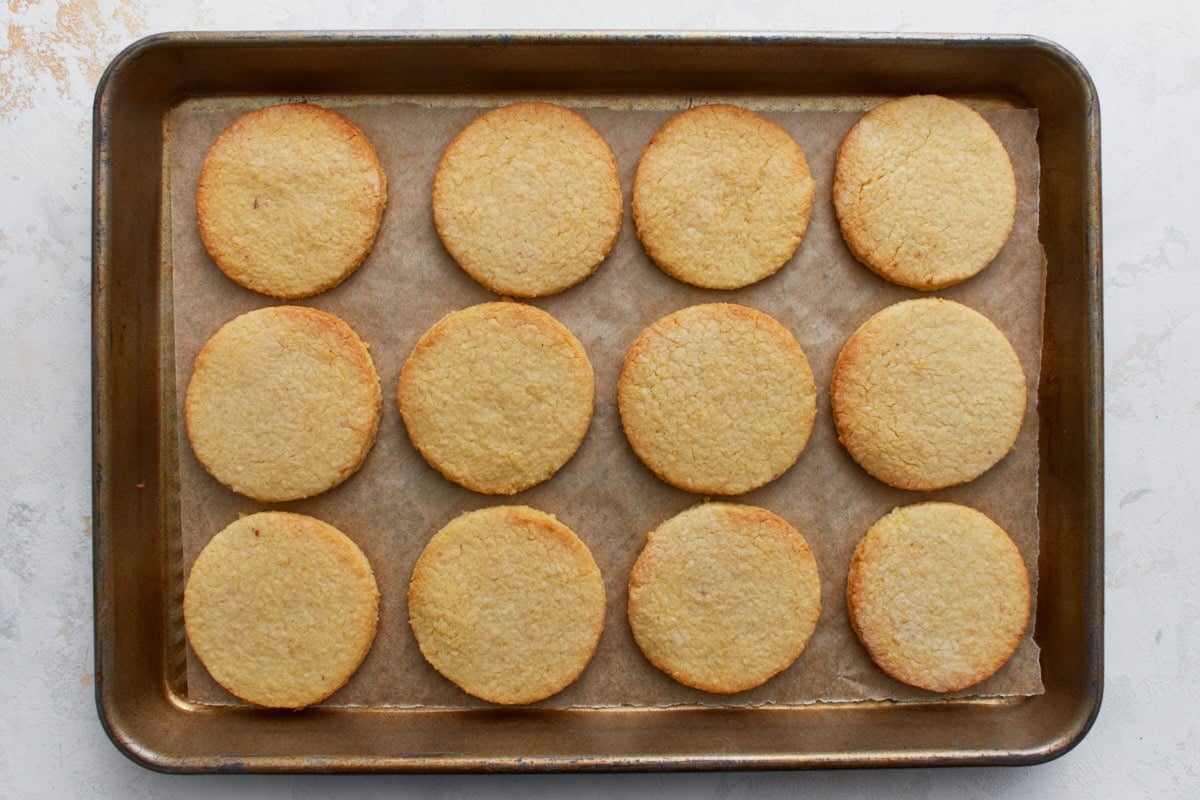 Freshly baked almond flour sugar cookies on a baking sheet with lightly golden edges.