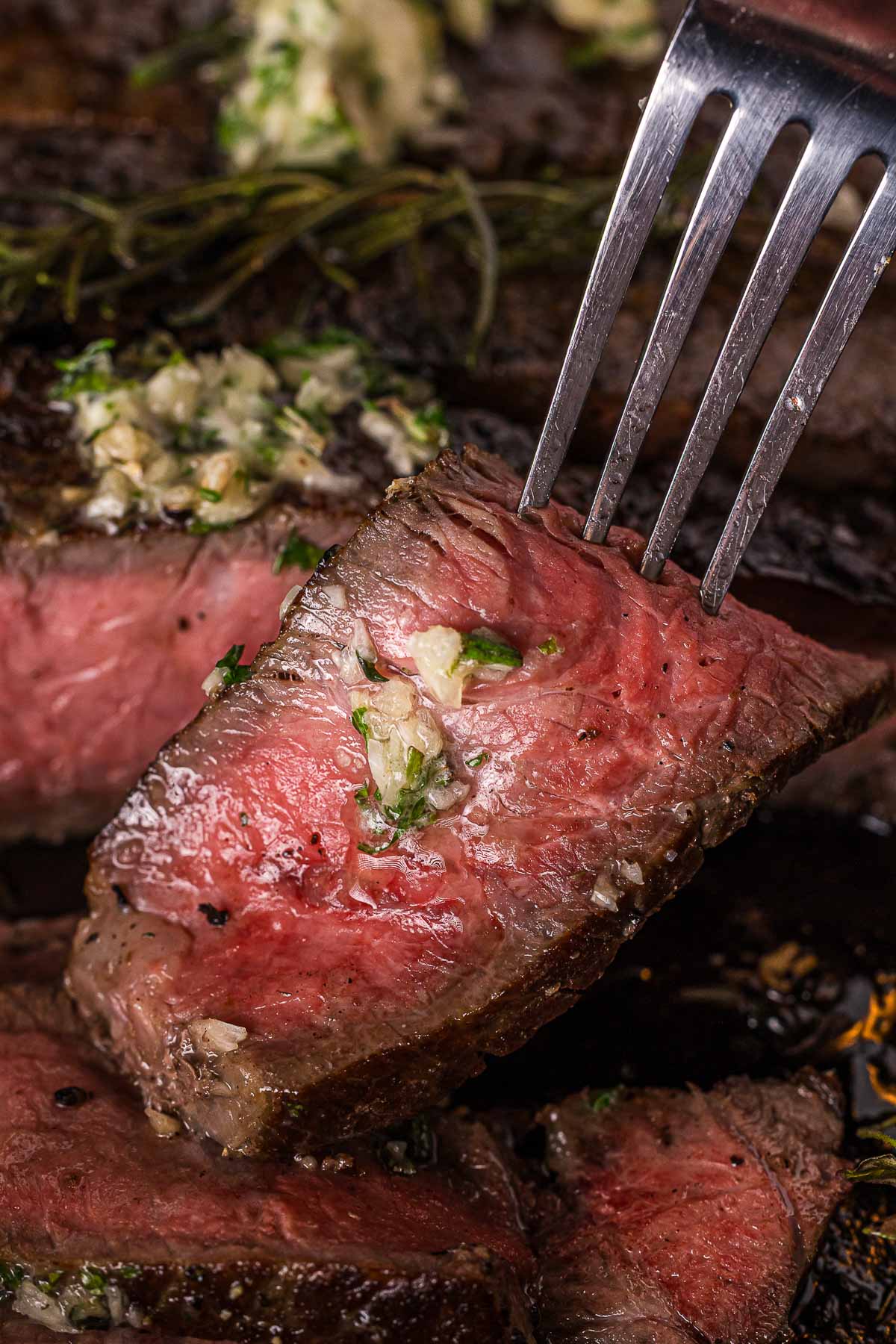 A close-up of a fork holding a juicy, medium-rare steak topped with garlic herb butter.