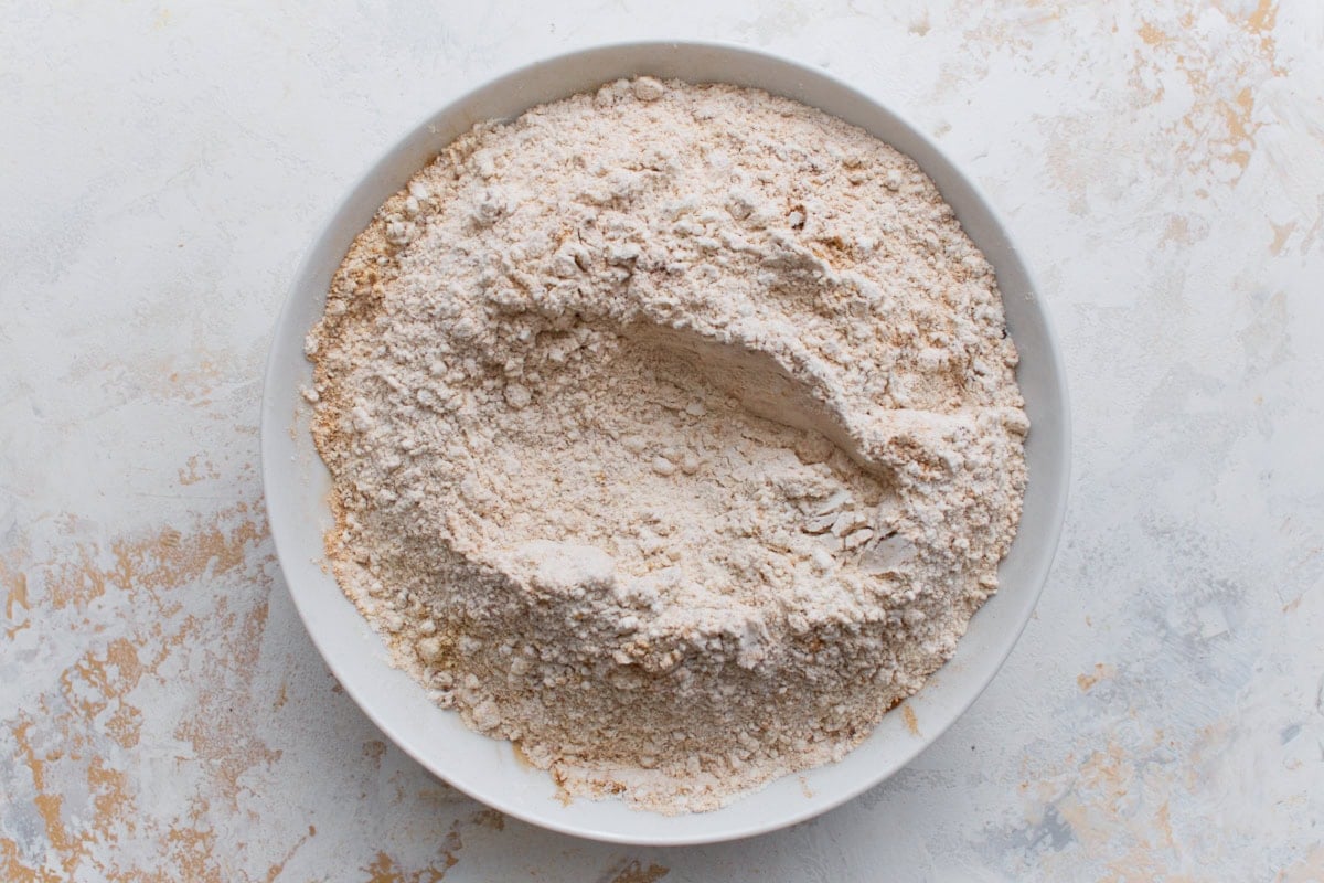 A white bowl filled with a blended mixture of gluten-free flour and warm spices like cinnamon and ginger on a light background.