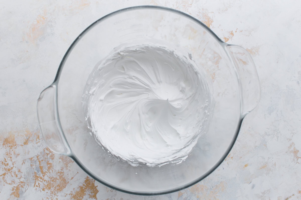 A glass mixing bowl filled with thick, smooth white royal icing whipped to stiff peaks, ready for piping.